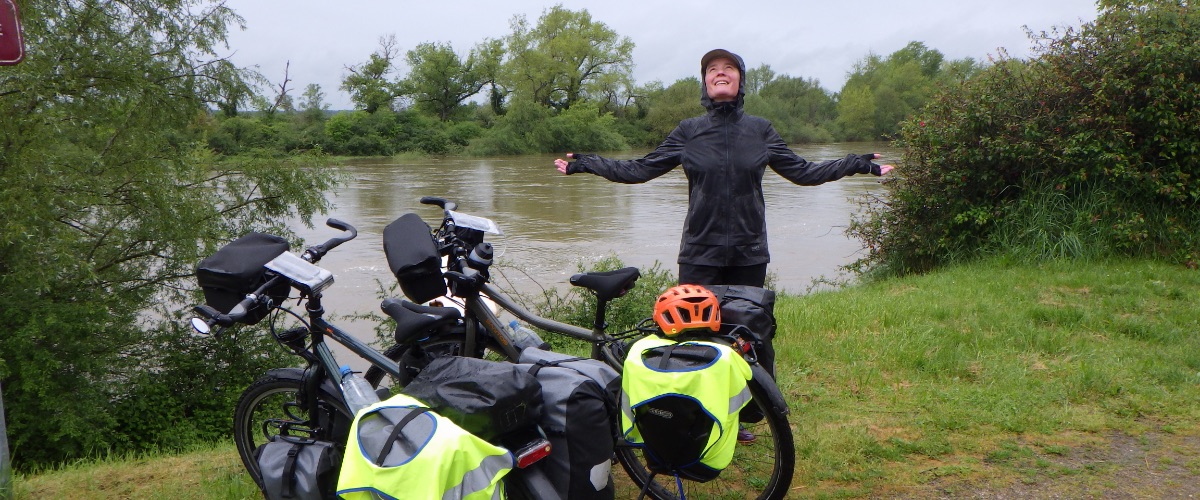 Saskia gehuld in regenkleding bij de fietsen langs de Loire met armen uitgespreid